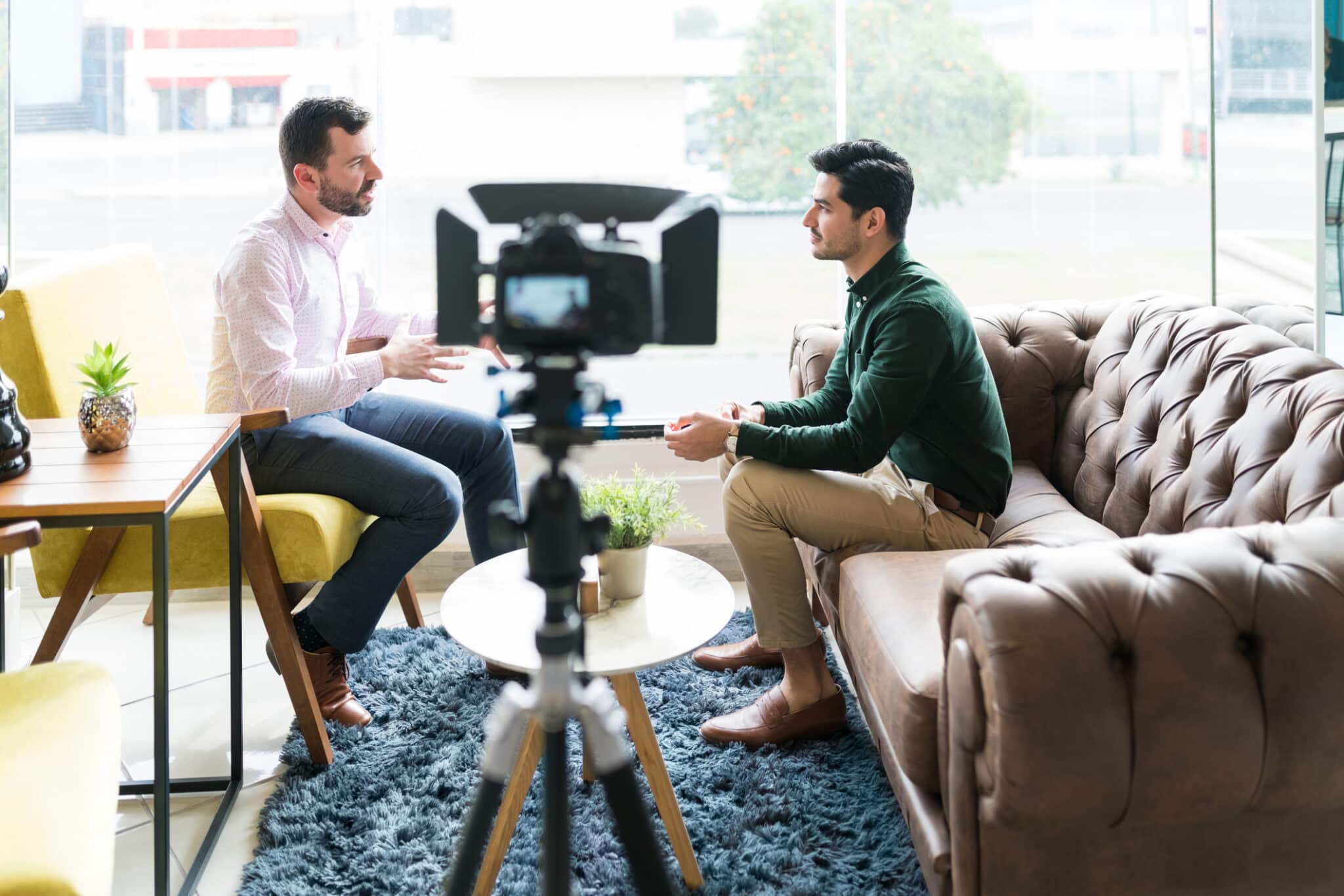 Hispanic journalist interviewing businessman while recording in video camera at office